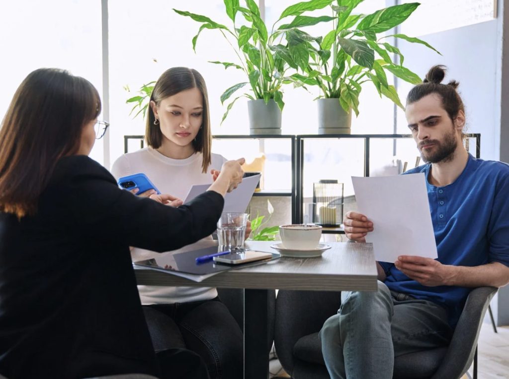 Couple comparing approximate home insurance cost quotes with insurance agent.